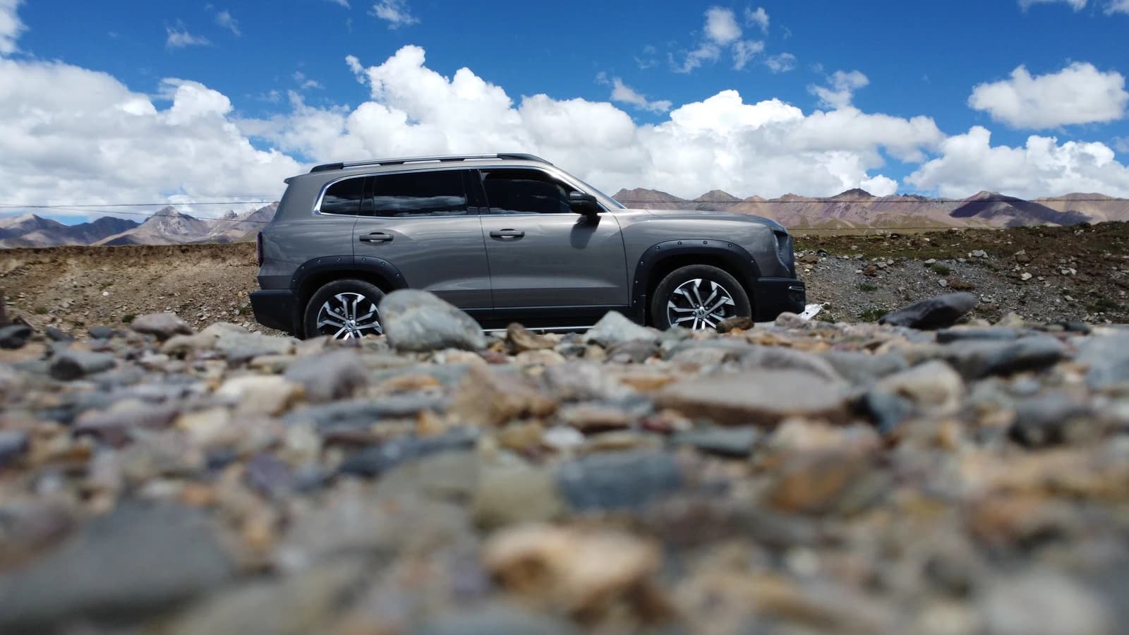 Overland SUV on stony plateau ground with mountain backdrop